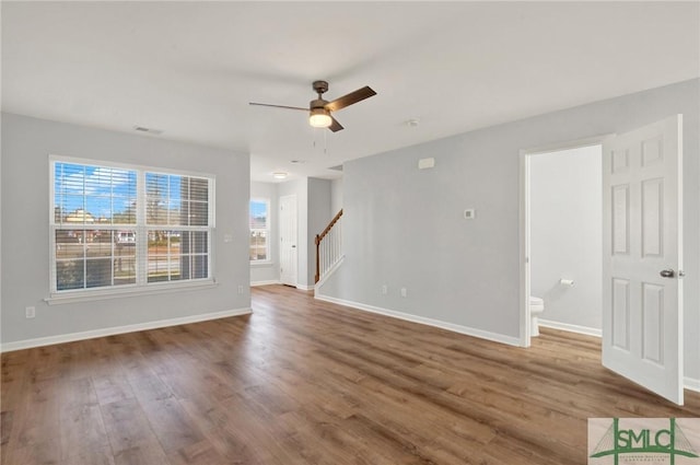 unfurnished living room with stairway, baseboards, ceiling fan, and wood finished floors