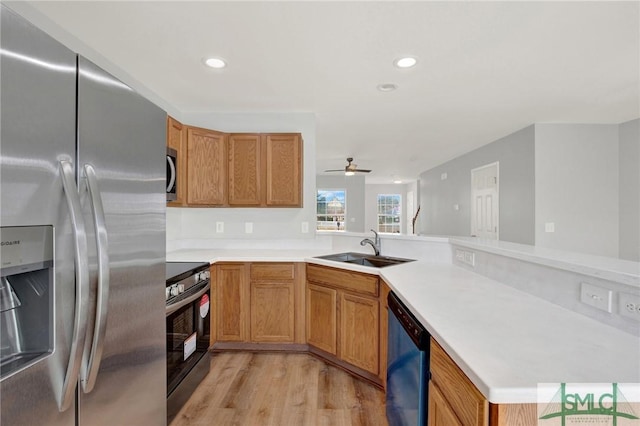 kitchen featuring light wood-type flooring, a sink, stainless steel appliances, a peninsula, and light countertops