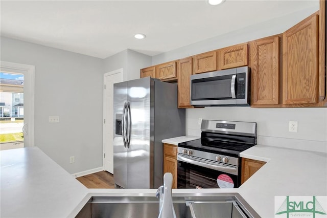 kitchen featuring light countertops, recessed lighting, wood finished floors, brown cabinetry, and stainless steel appliances