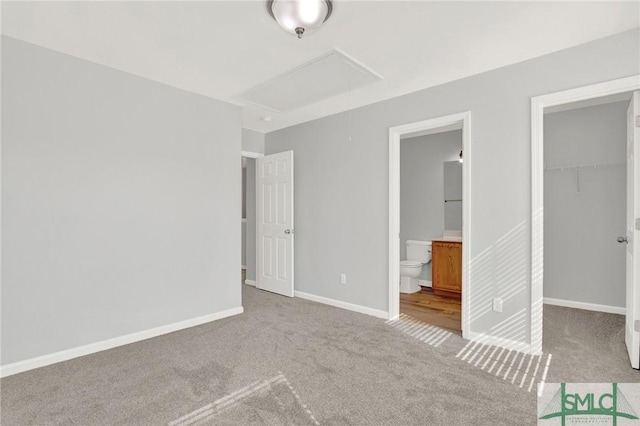 unfurnished bedroom featuring a walk in closet, baseboards, carpet, ensuite bathroom, and a closet