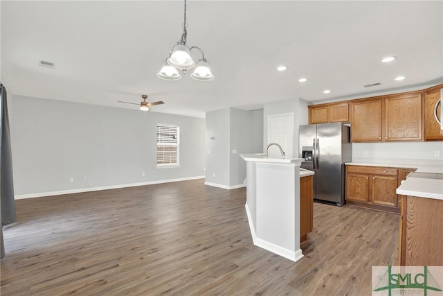 kitchen featuring a center island with sink, stainless steel refrigerator with ice dispenser, wood finished floors, recessed lighting, and light countertops