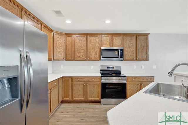 kitchen featuring light wood-type flooring, visible vents, a sink, stainless steel appliances, and light countertops