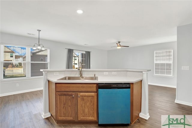 kitchen with a center island with sink, ceiling fan with notable chandelier, a sink, light countertops, and dishwashing machine