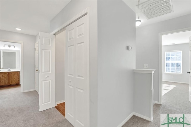 hall featuring visible vents, light carpet, and baseboards