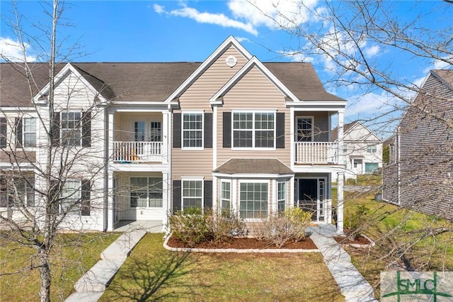 view of front of property featuring a front yard, a balcony, and a shingled roof