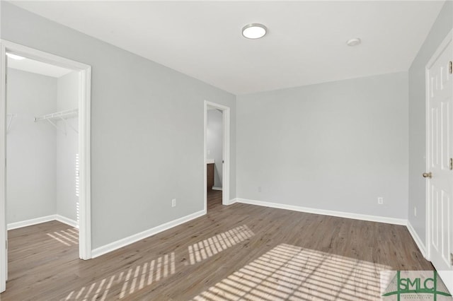 unfurnished bedroom featuring a walk in closet, wood finished floors, and baseboards