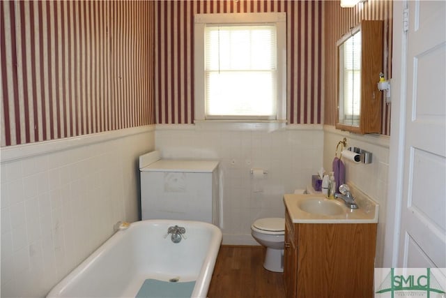 full bathroom with toilet, wainscoting, wallpapered walls, a freestanding bath, and vanity