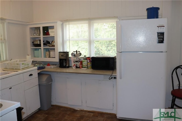 kitchen featuring black microwave, light countertops, freestanding refrigerator, brick floor, and white cabinetry