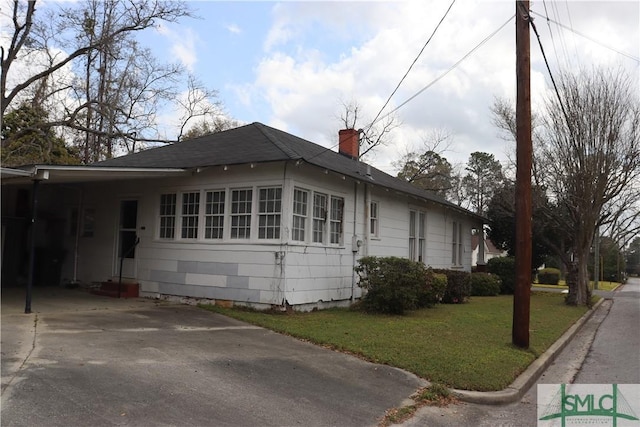 view of home's exterior featuring a yard, concrete driveway, a shingled roof, a carport, and a chimney