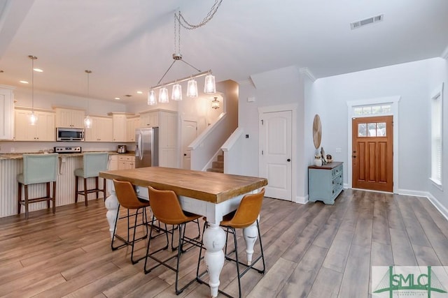 dining room featuring visible vents, baseboards, recessed lighting, stairway, and wood finished floors