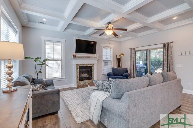 living area featuring a glass covered fireplace, visible vents, beamed ceiling, and wood finished floors