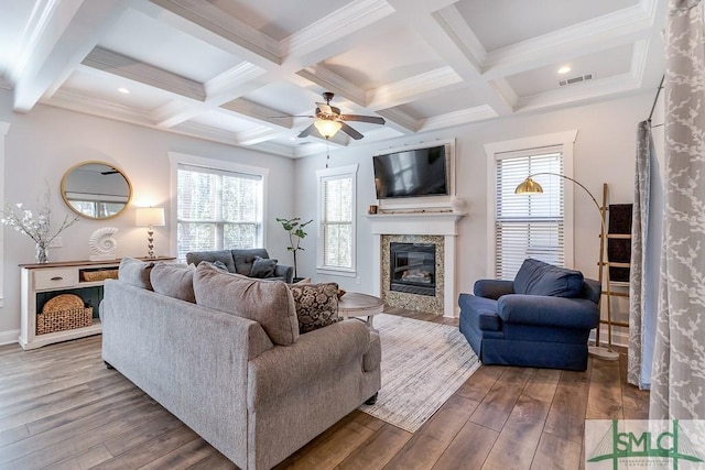 living area with beamed ceiling, a ceiling fan, hardwood / wood-style floors, and a glass covered fireplace