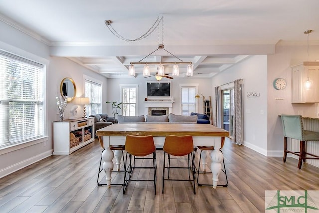 kitchen with baseboards, a fireplace, a kitchen bar, beam ceiling, and wood finished floors