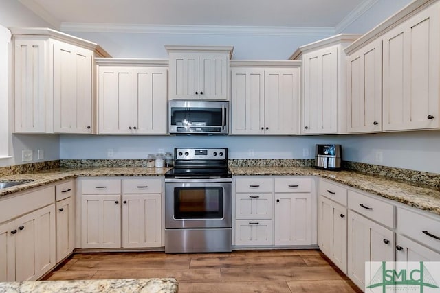 kitchen featuring light wood-style flooring, crown molding, light stone counters, and appliances with stainless steel finishes