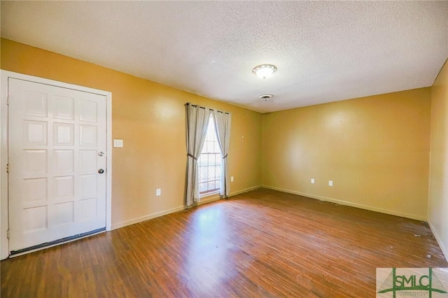 empty room with wood finished floors, baseboards, and a textured ceiling