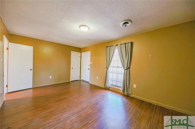 spare room with baseboards, a textured ceiling, and wood finished floors