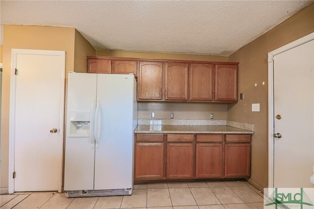 kitchen featuring light tile patterned floors, brown cabinets, white fridge with ice dispenser, and a textured ceiling