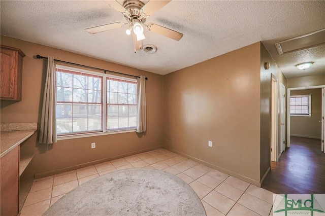 empty room with visible vents, a textured ceiling, light tile patterned flooring, baseboards, and ceiling fan