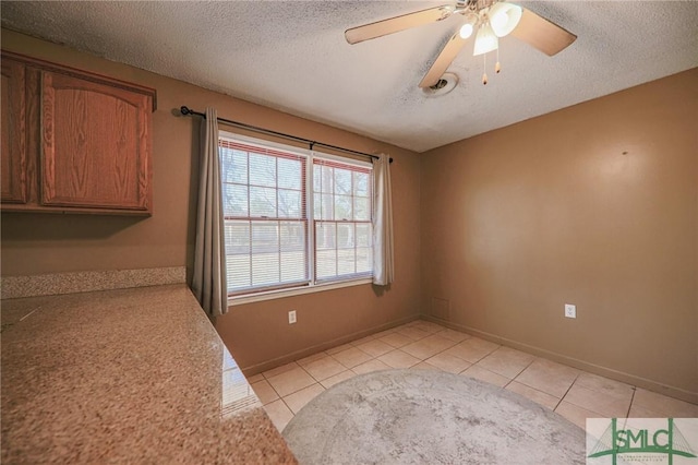 interior space with ceiling fan, baseboards, a textured ceiling, and light tile patterned flooring