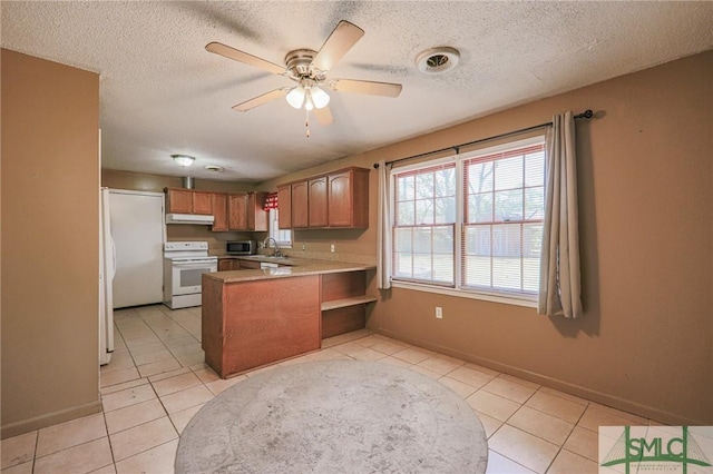 kitchen with stainless steel microwave, under cabinet range hood, light countertops, a peninsula, and white range with electric stovetop
