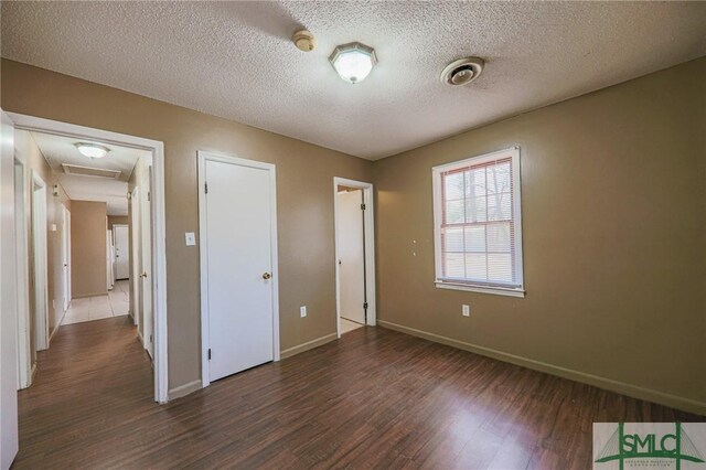 unfurnished bedroom featuring baseboards, a textured ceiling, attic access, and wood finished floors