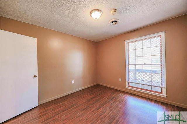 empty room featuring a textured ceiling, baseboards, and wood finished floors
