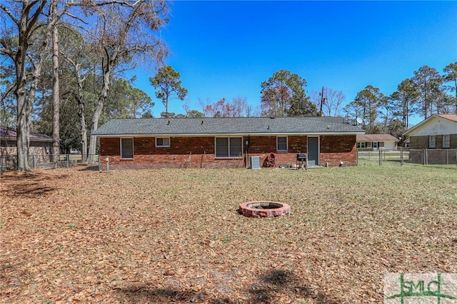 rear view of house with a yard, a fire pit, and fence