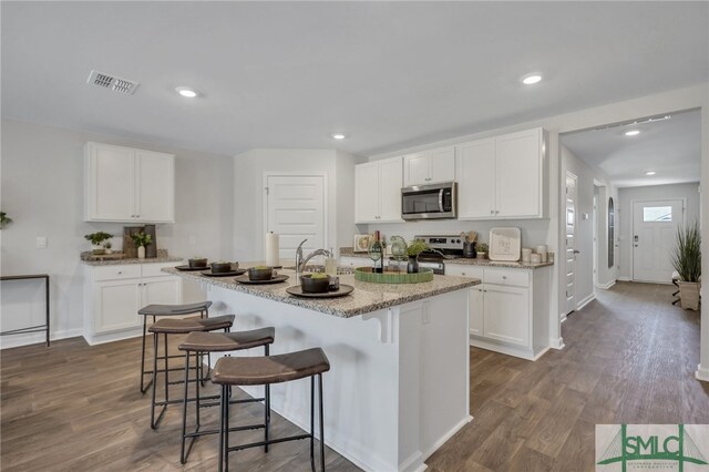 kitchen featuring stainless steel appliances, a kitchen bar, visible vents, and dark wood finished floors