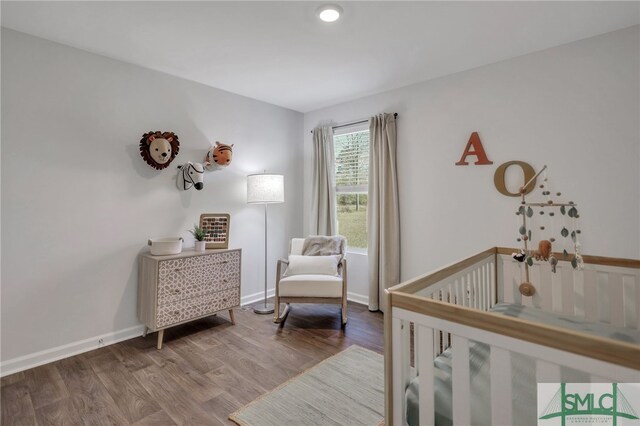 bedroom with baseboards, a nursery area, and wood finished floors