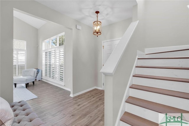 staircase with a notable chandelier, wood finished floors, and baseboards