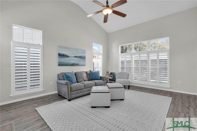 living area with baseboards, high vaulted ceiling, a ceiling fan, and wood finished floors