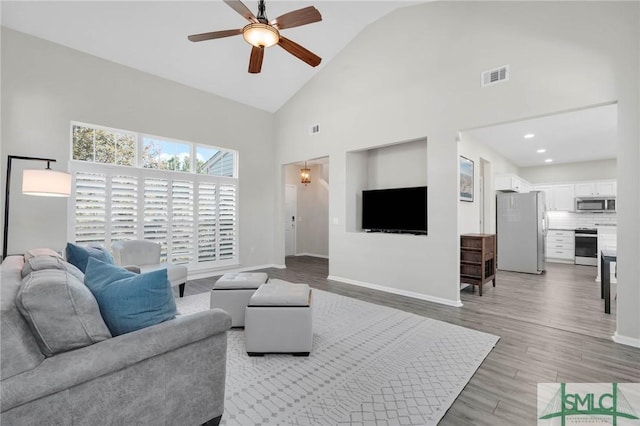 living room with baseboards, visible vents, high vaulted ceiling, ceiling fan, and light wood-style floors