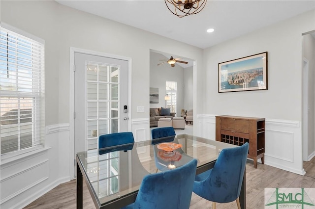 dining space with recessed lighting, ceiling fan with notable chandelier, wainscoting, and light wood finished floors