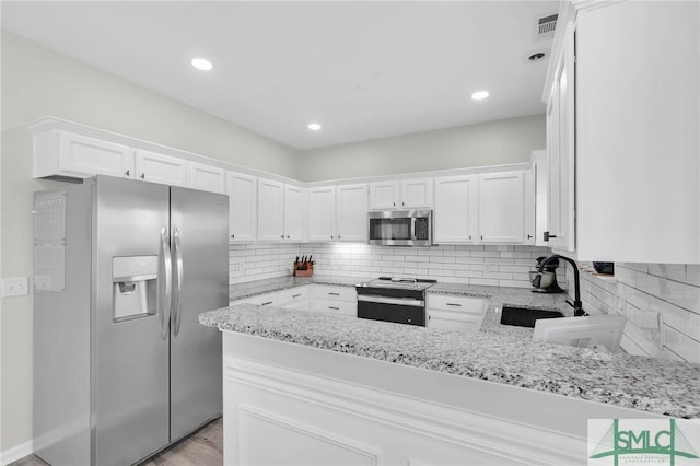 kitchen featuring light stone countertops, a peninsula, a sink, appliances with stainless steel finishes, and white cabinetry