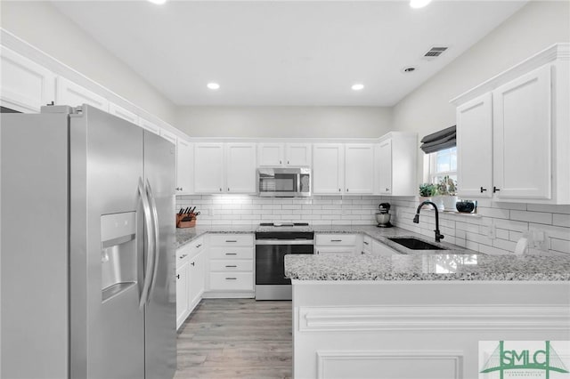 kitchen with appliances with stainless steel finishes, white cabinetry, a peninsula, and a sink