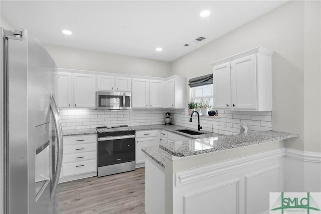kitchen featuring light stone countertops, a peninsula, white cabinets, stainless steel appliances, and a sink