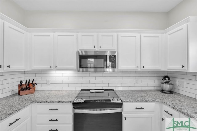 kitchen with tasteful backsplash, appliances with stainless steel finishes, white cabinetry, and light stone countertops