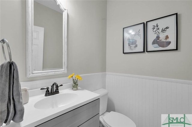 half bath with vanity, wainscoting, and toilet