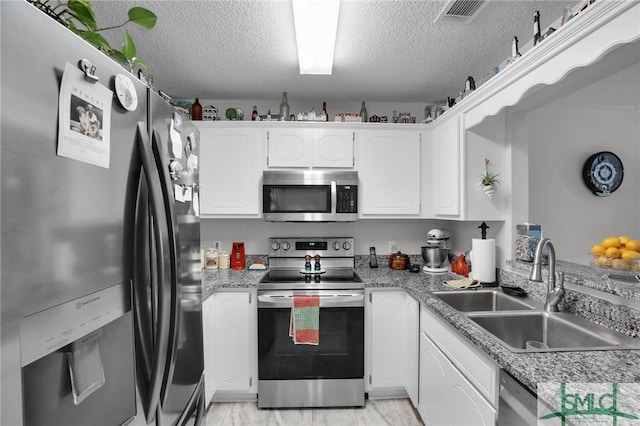 kitchen with visible vents, a sink, a textured ceiling, stainless steel appliances, and white cabinets