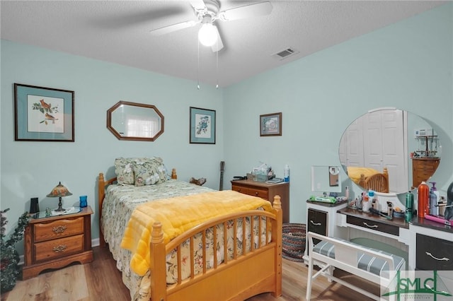 bedroom featuring a ceiling fan, wood finished floors, visible vents, and a textured ceiling