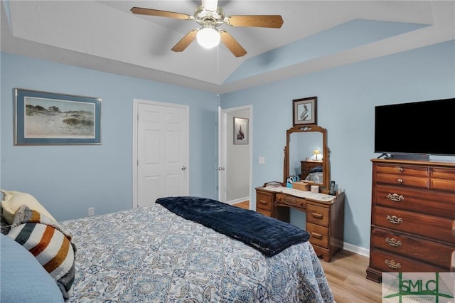 bedroom with a ceiling fan, baseboards, light wood finished floors, a tray ceiling, and vaulted ceiling