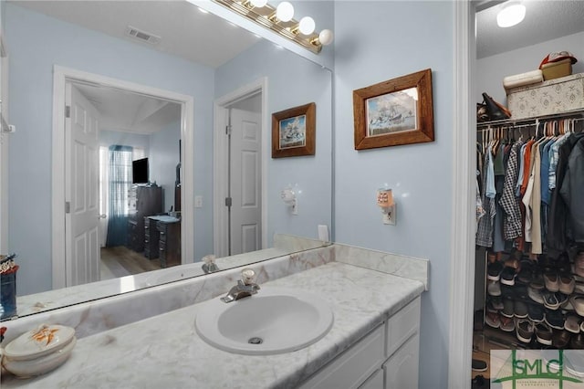 bathroom with vanity, a walk in closet, and visible vents