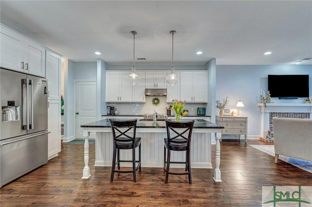 kitchen with dark countertops, a breakfast bar area, high quality fridge, and under cabinet range hood