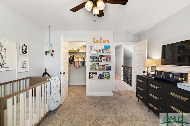 bedroom with light colored carpet, a walk in closet, a closet, ceiling fan, and baseboards