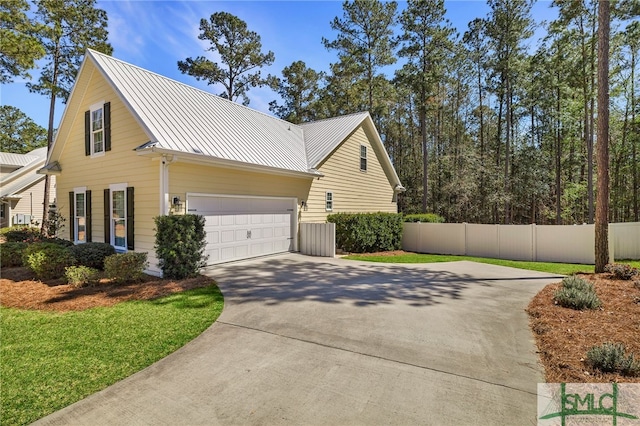 view of side of home featuring concrete driveway, fence, metal roof, a standing seam roof, and a garage