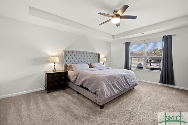 carpeted bedroom with a tray ceiling, baseboards, visible vents, and a ceiling fan