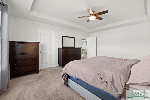 bedroom with a tray ceiling, light colored carpet, and a ceiling fan