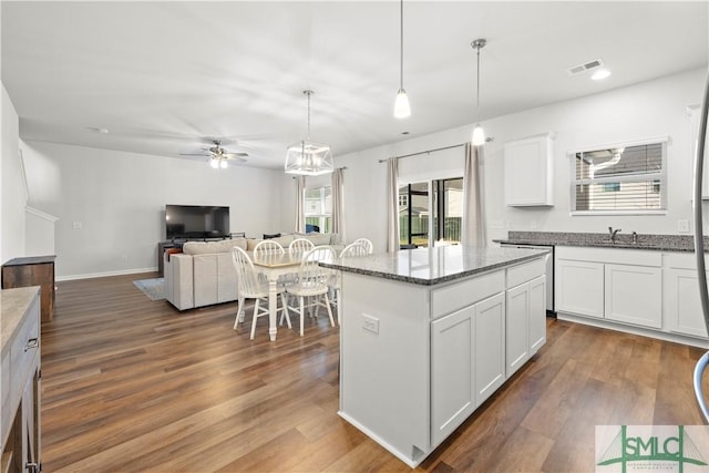 kitchen with dark wood-style floors, a ceiling fan, visible vents, a kitchen island, and white cabinetry