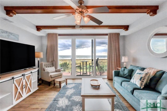 living area with beamed ceiling, light wood-type flooring, and ceiling fan