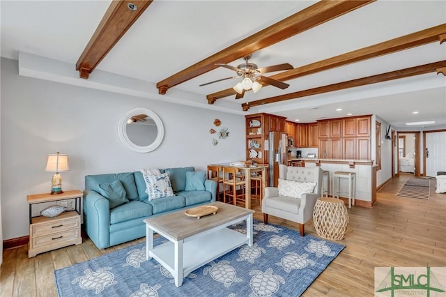 living area with beamed ceiling, baseboards, light wood-type flooring, and a ceiling fan